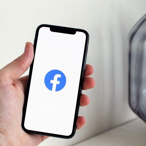 Close-up of a hand holding a smartphone displaying the Facebook logo indoors.